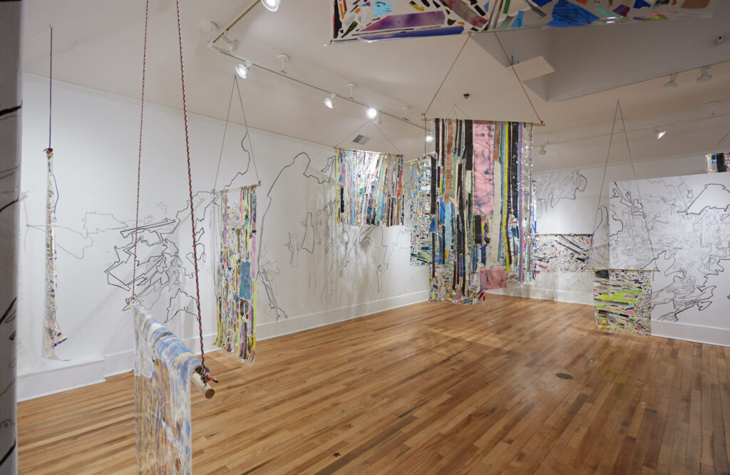 gallery exhibition featuring patchworked paintings hung on the walls and from the ceiling