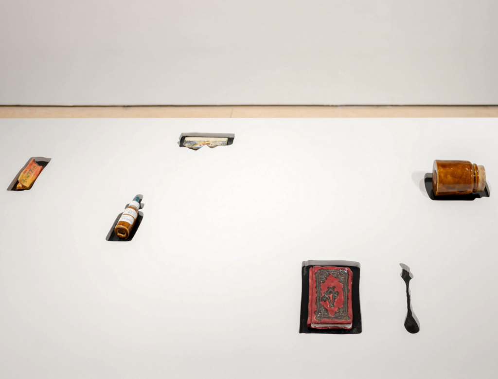 Antique everyday items, including a comb and a pill jar, protrude from a pristine white surface, each object frozen mid-emergence from the table.