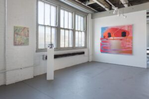 Two white gallery walls, the left one with three rectangular windows and natural light beaming inside. A pedestal with a mushroom-shaped sculpture sits in front of it, with an abstract colorful winding landscape on canvas on the wall beside it.