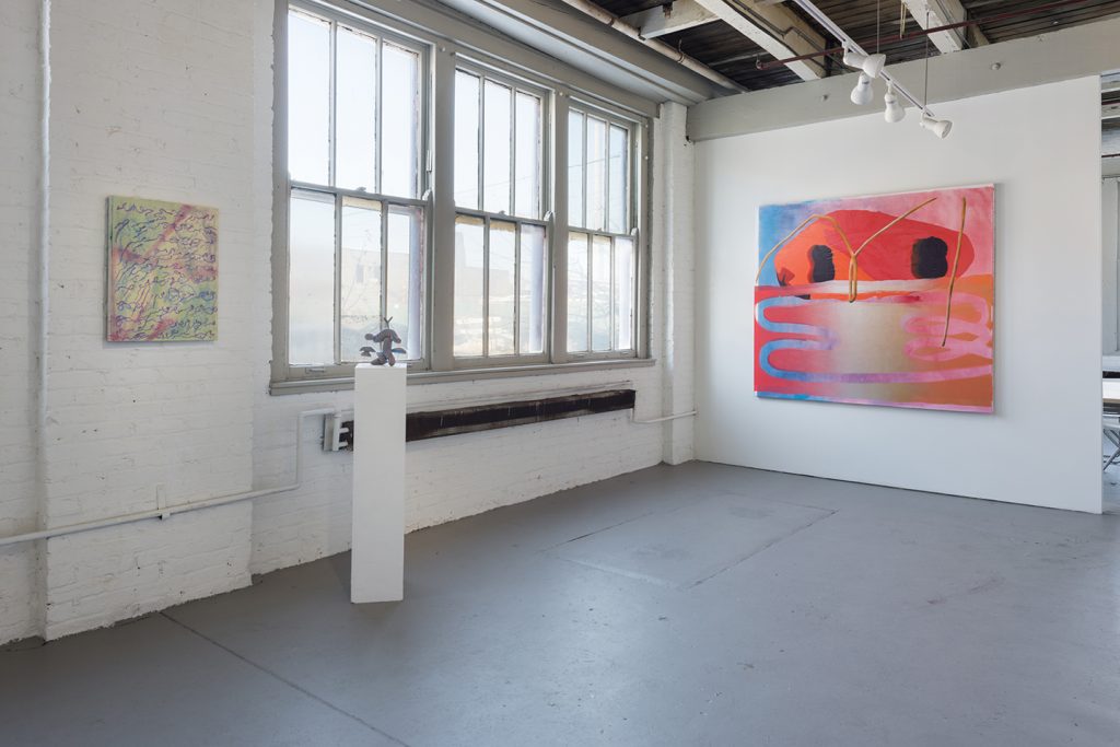 Two white gallery walls, the left one with three rectangular windows and natural light beaming inside. A pedestal with a mushroom-shaped sculpture sits in front of it, with an abstract colorful winding landscape on canvas on the wall beside it.