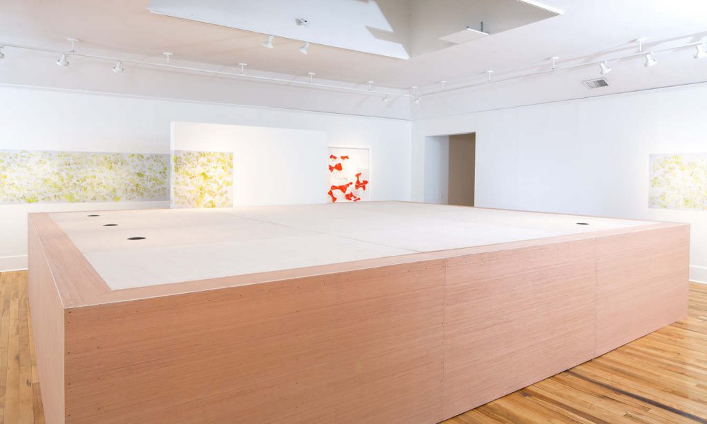 art gallery exhibition of various photographs and large wooden form in the center of the space