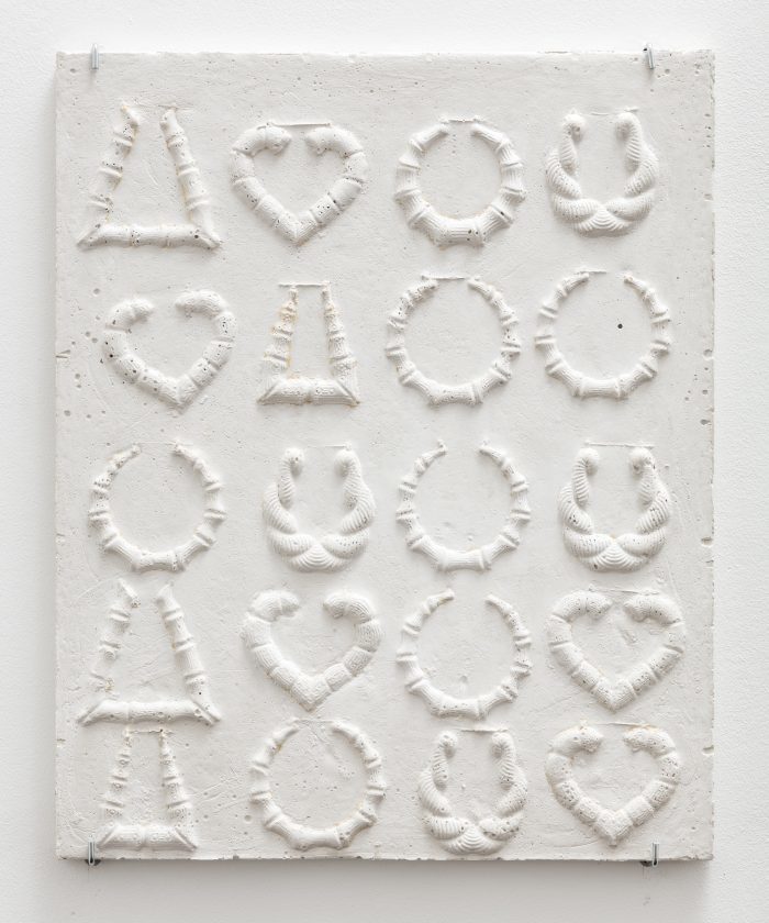 A relief on white stone of 20 different earring patterns ranging in shape from circles to hearts.