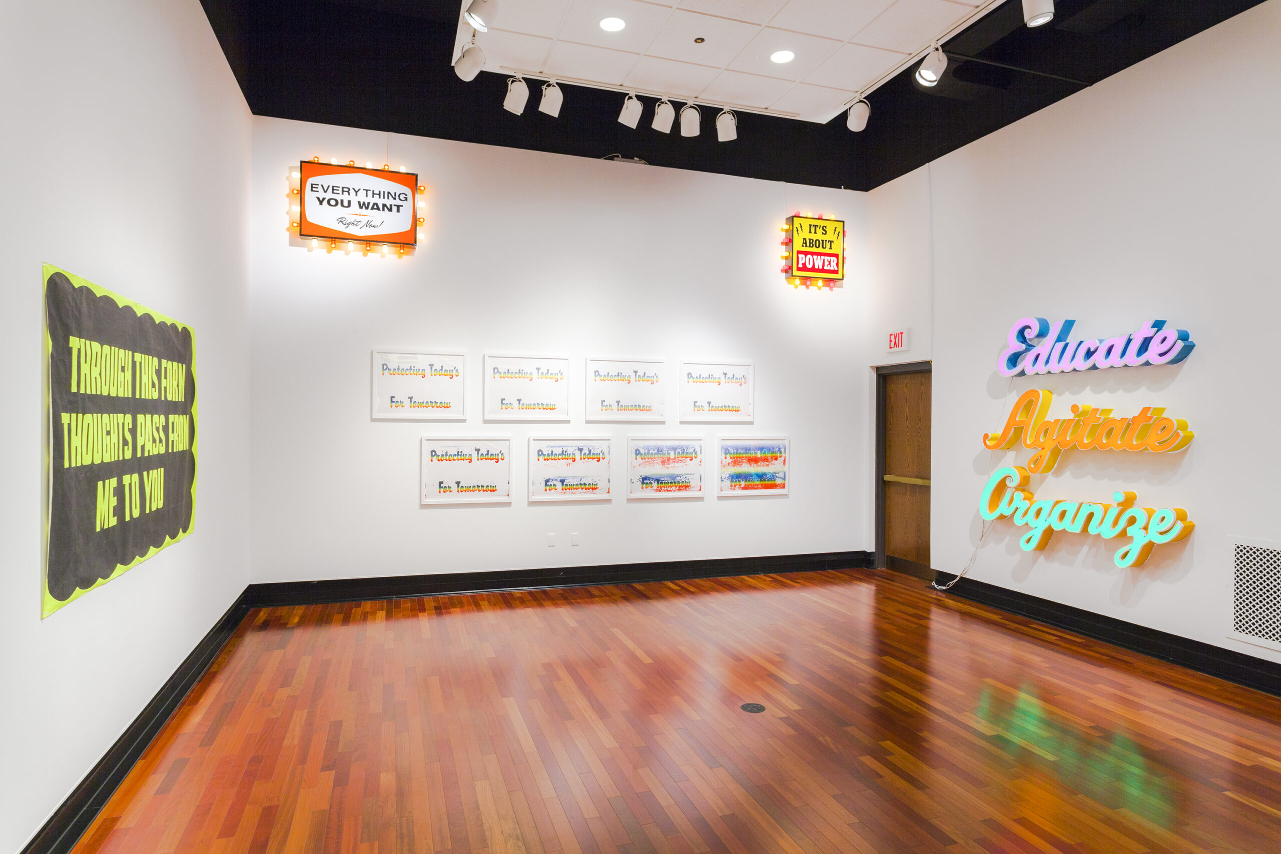White walls with different signs on each, including eight white framed signs in two rows of four reading PROTECTING TODAY'S FOR TOMORROW in rainbow colors.