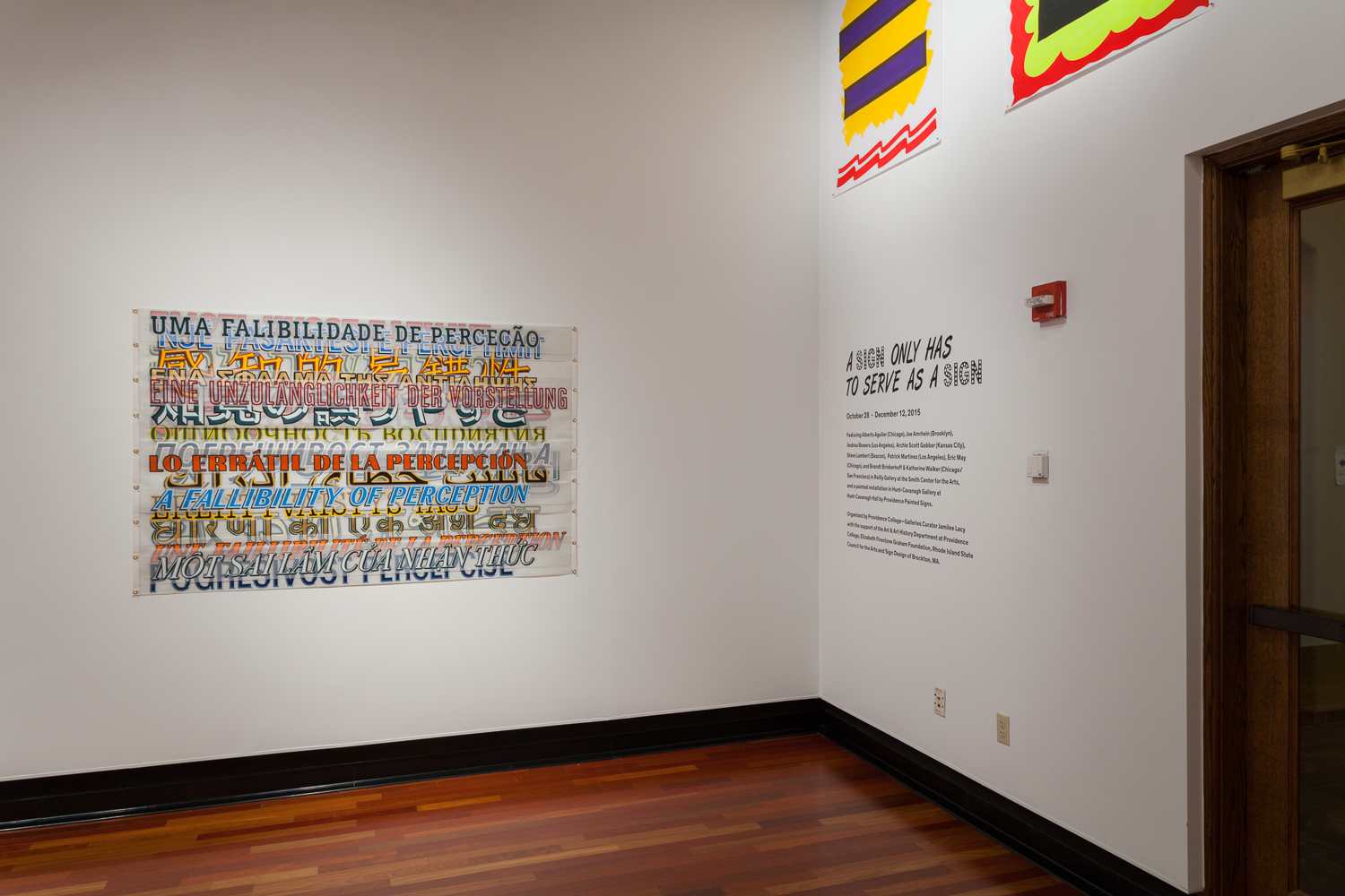 Installation view of an artwork on the wall with the words A FALLIBILITY OF PERCEPTION overlapping in many different languages. To the right are words reading A SIGN ONLY HAS TO SERVE AS A SIGN below two abstract artworks.