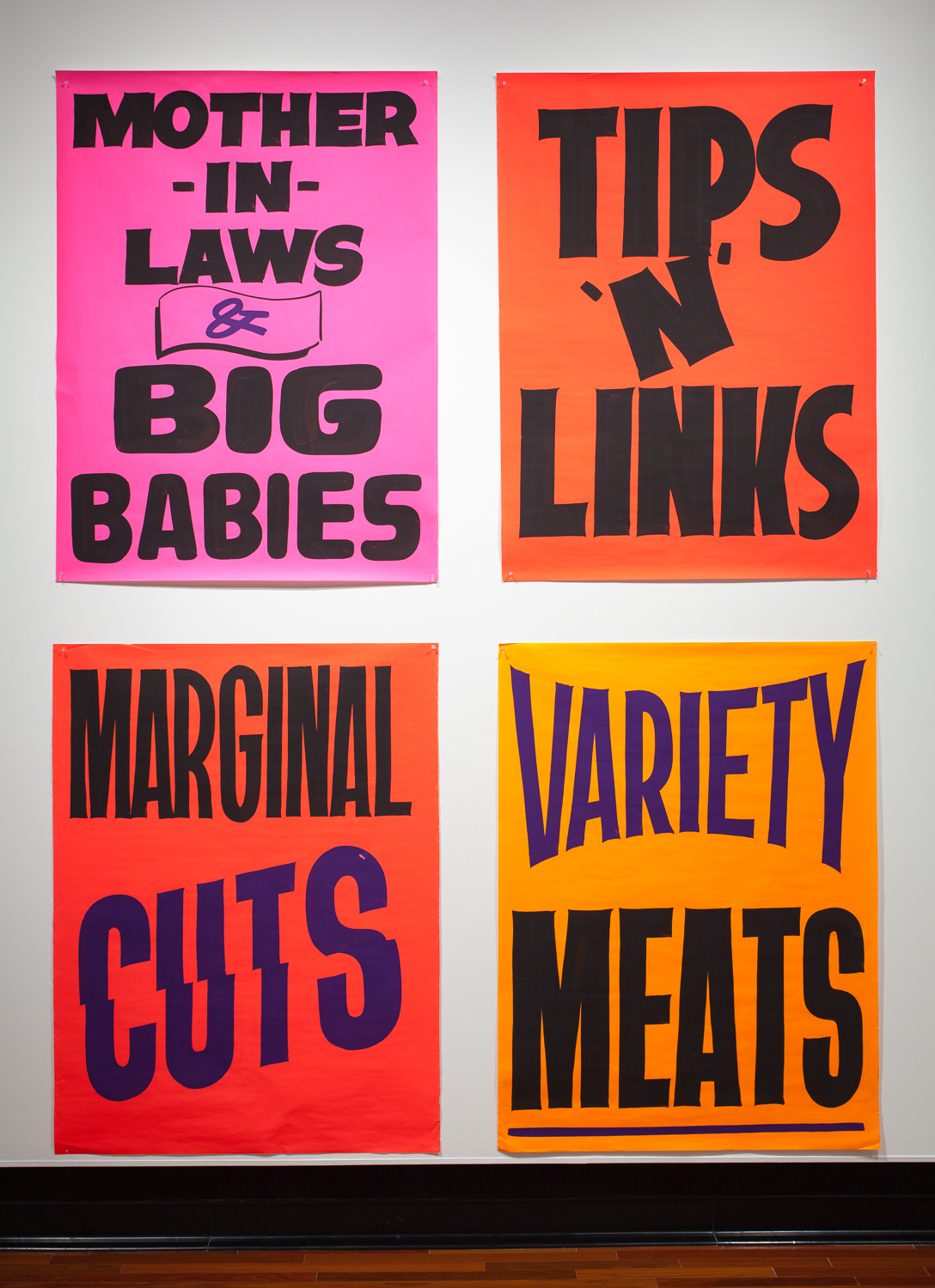 Four bright posters in a 2x2 arrangment with large lettering. From left to right they read MOTHER IN LAWS & BIG BABIES, TIPS N LINKS, MARGINAL CUTS, VARIETY MEATS.