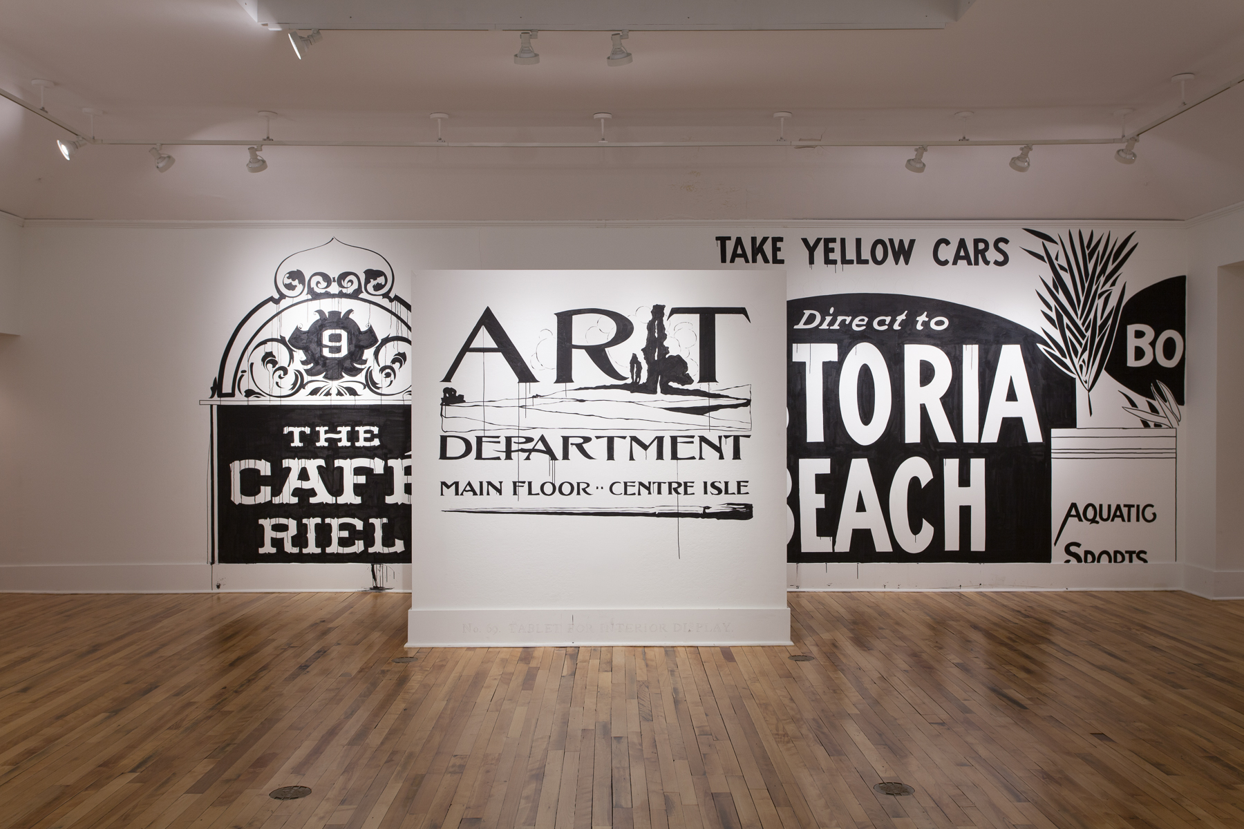 Installation view of a small white wall covered in the large black words ART DEPARTMENT MAIN FLOOR CENTRE ISLE. Behind is a larger wall with more large black and white signs painted directly onto it.