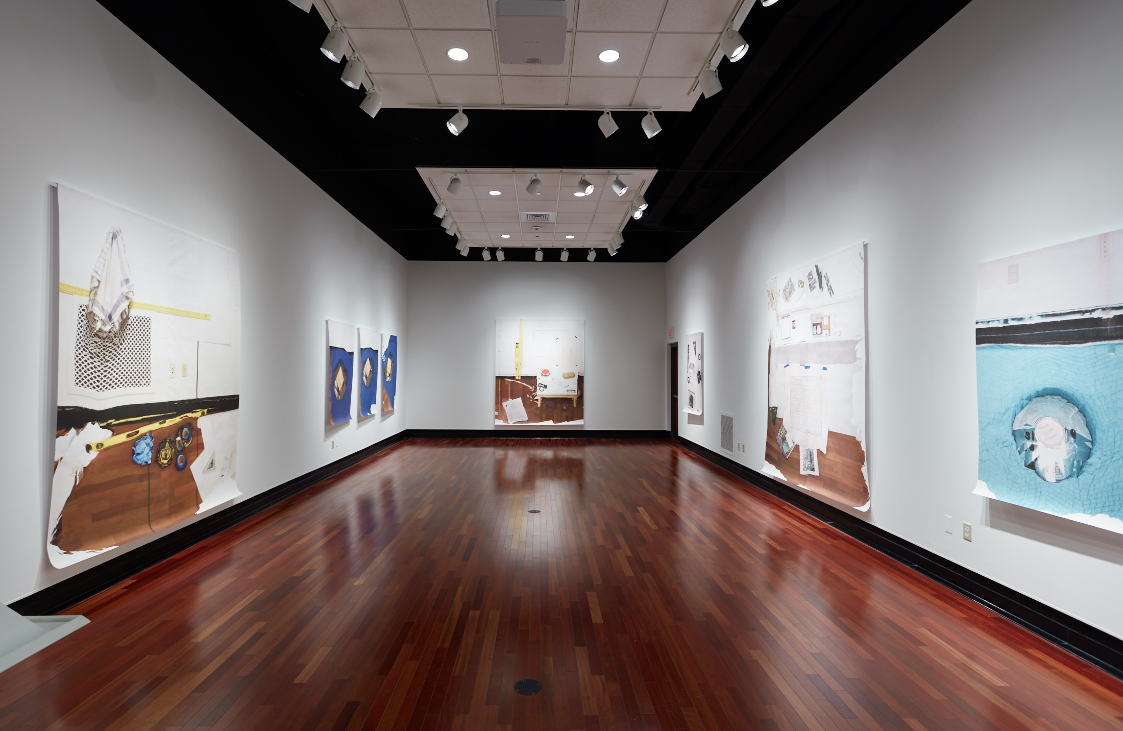 Nine large works on paper along three walls of an art gallery.