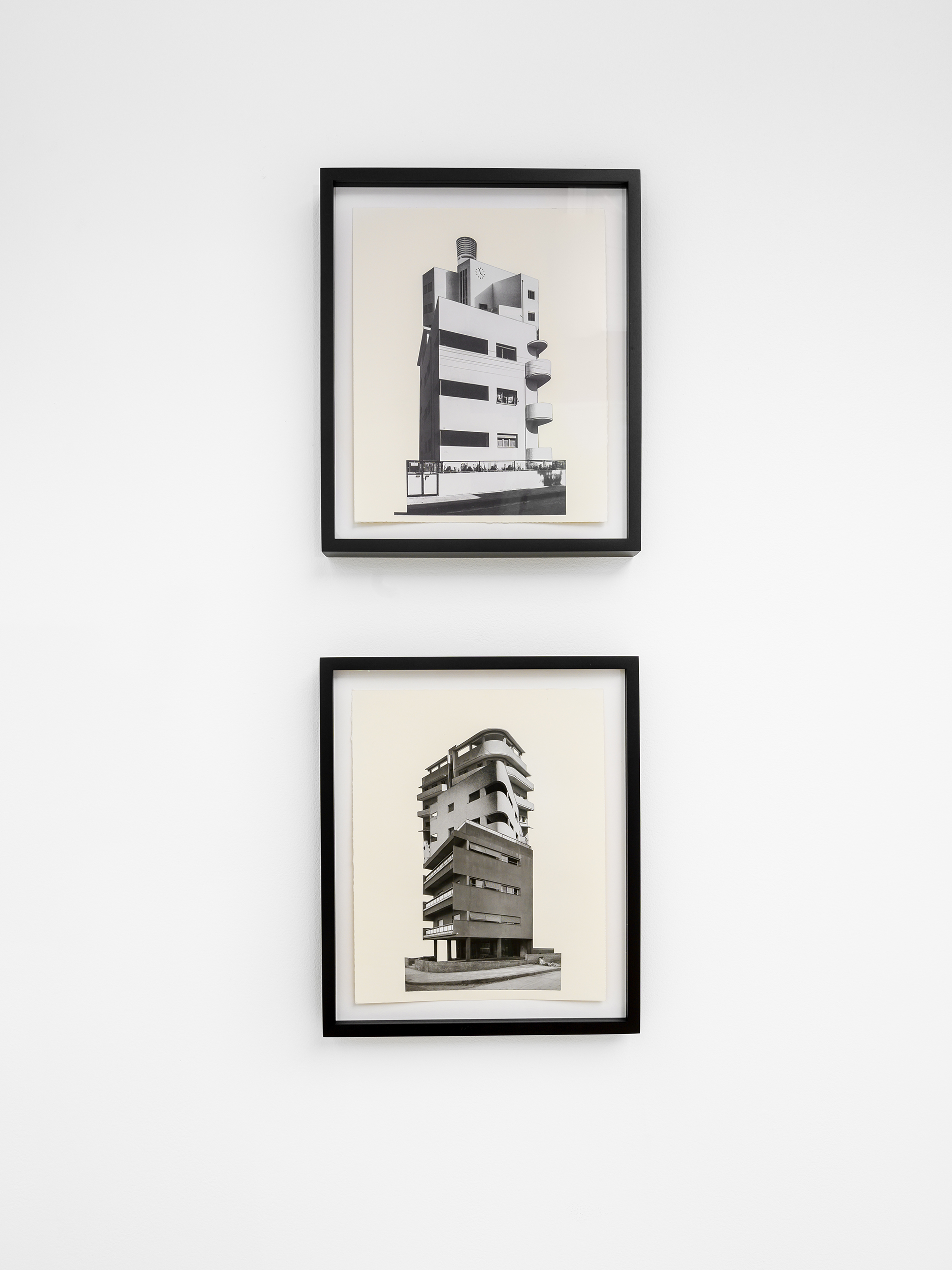 Two black frames, one above the other, hold photographs of two buildings, the first showing a four-story building with square floors and circular balconies, the second below it showing a six-story building made of two large squares stacked above each other
