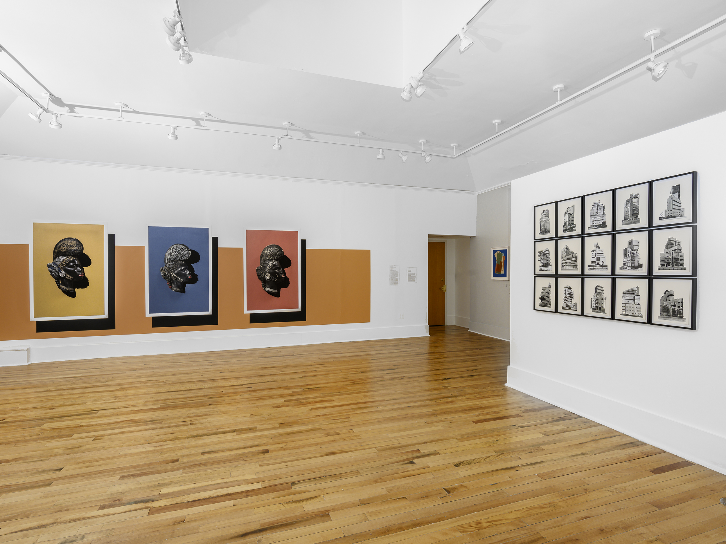 Installation view of two walls: one with a large orange stripe behind three artworks of a figure's head, each with a bright background, the other a 3x5 array of architectural photographs.