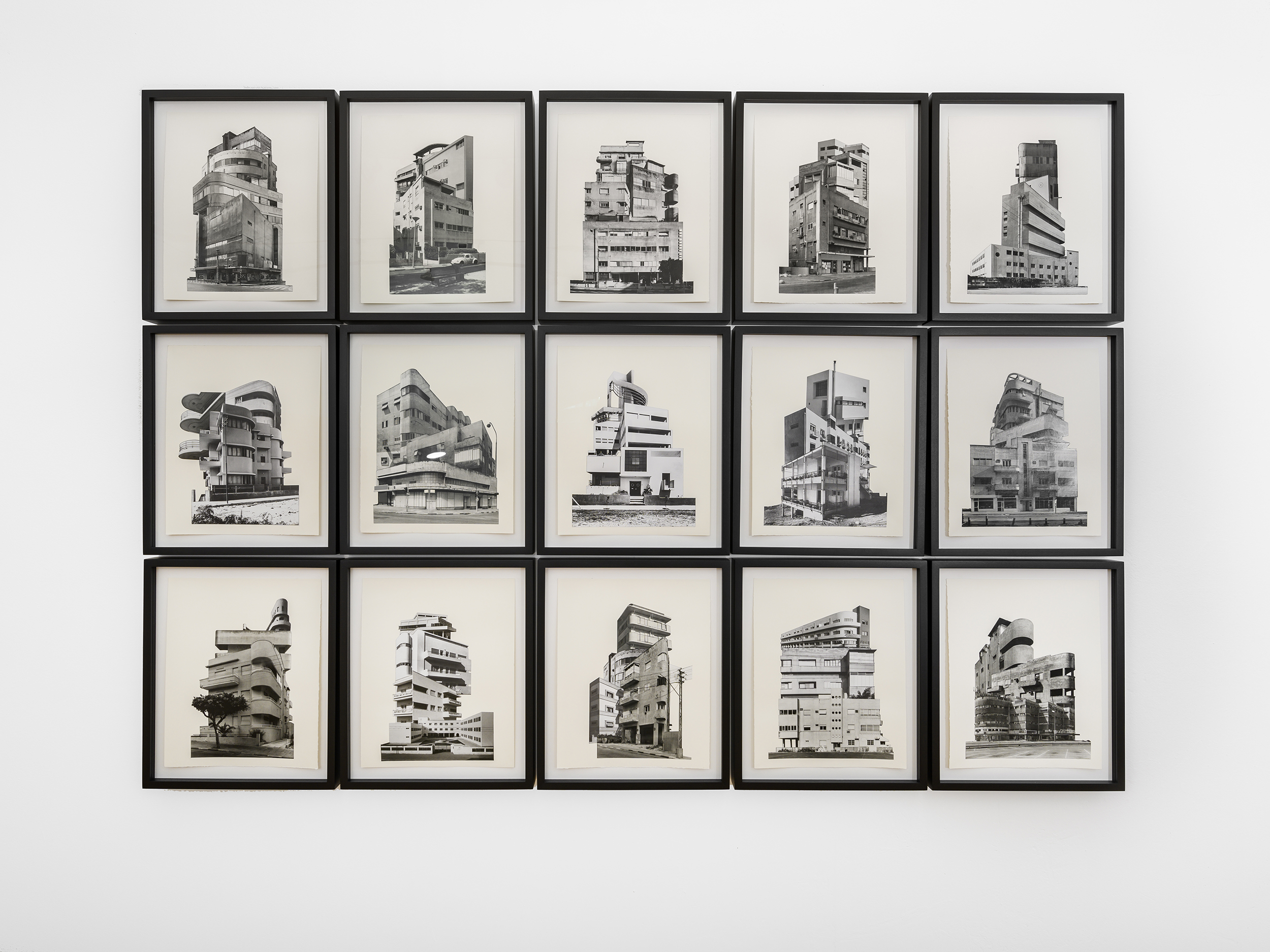 An 3x5 array of artworks framed in black. Each depicts photograph of a different building in black and white on a blank white background.