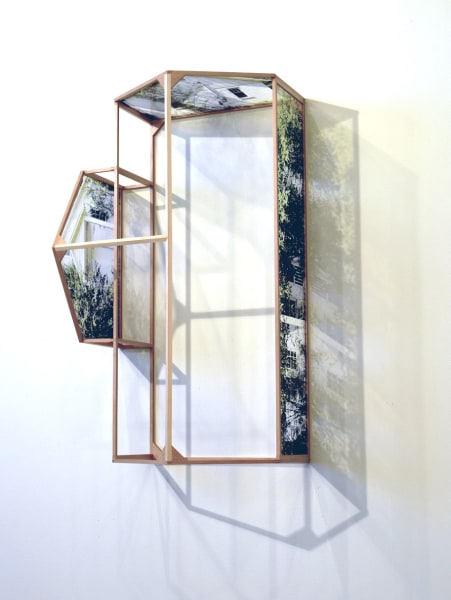 Side view of a wooden house frame mounted to a white wall. Three walls are represented by transparent photographs of a white, vinyl sided house fitting the same dimensions as the frame.
