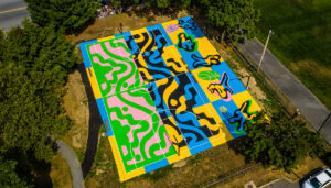 Aerial view of a brightly patterned basketball couty. The court is split into two halves, one bubblegum pink and lime green, while the other is yellow and blue.