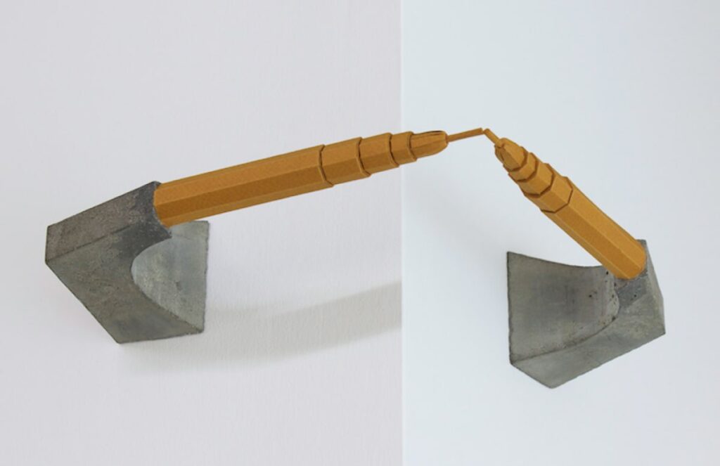 A sculpture with two brown buildings reminiscent of miniature skyscrapers facing each other horizontally. They are mirror images of one another, both mounted on stands of grey concrete.