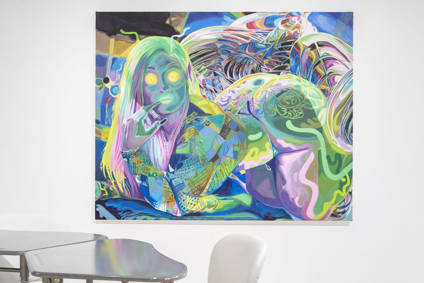 Painting of a green and purple figure with long hair and yellow circles for eyes touching their mouth. Two gray desks and a white chair sit in front of the painting.