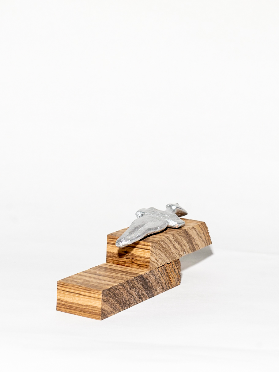 Two rectangular blocks of wood are stacked like stairs on top of each other. A silver figurine lies flat on the top block, looking like a simplified human figure.