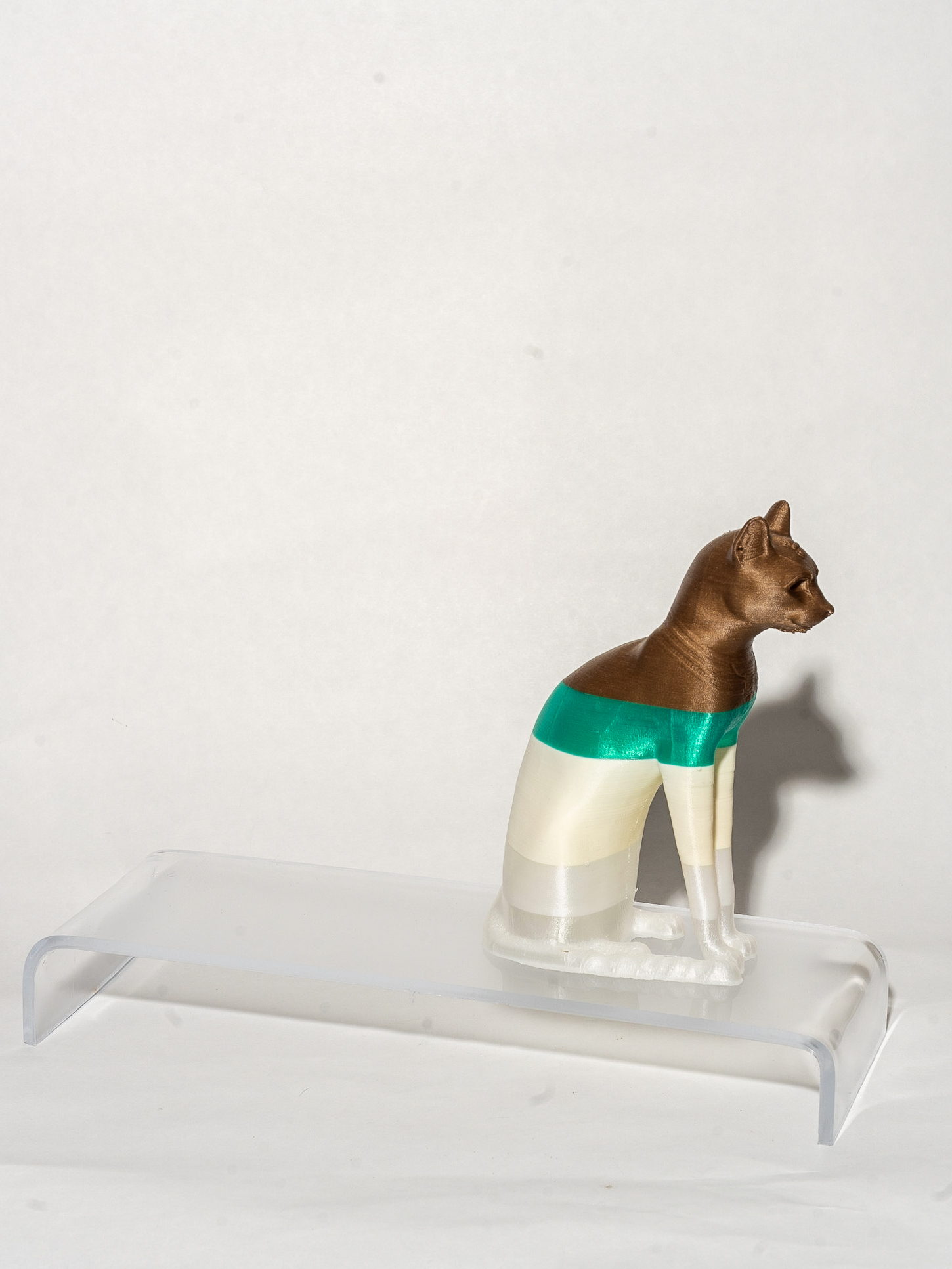A figure of a cat sitting in profile on its hind legs sits on top of a clear rectangular stand. The cat is colored with horizontal stripes.