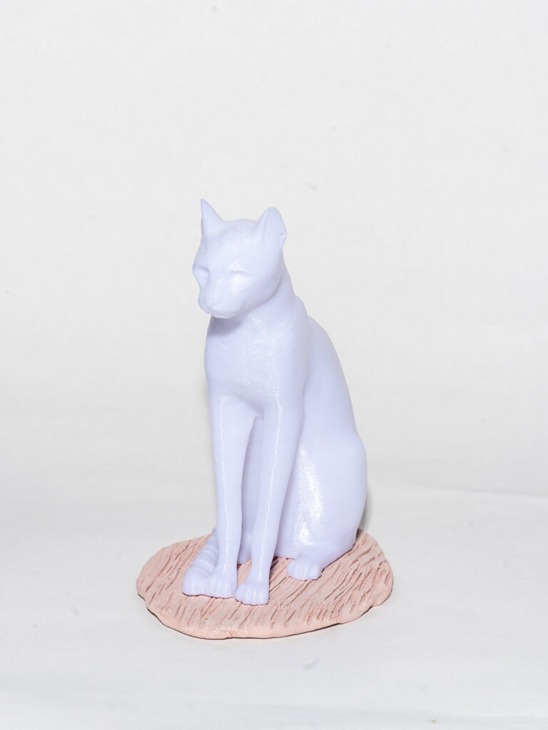 A 3D figure of a cat sits on top of a beige circle of clay carved with lines. The cat is completely white with no detail defining its features.