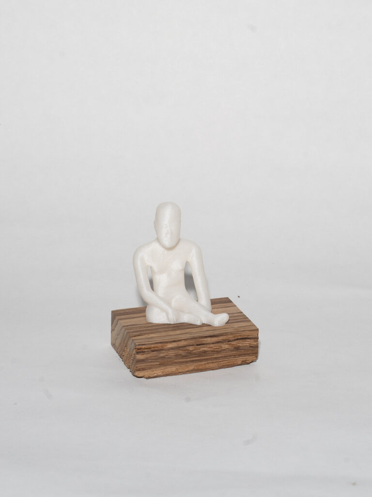 A 3D human figure sits on a rectangular wooden block. The figure is entirely white with limited detail.