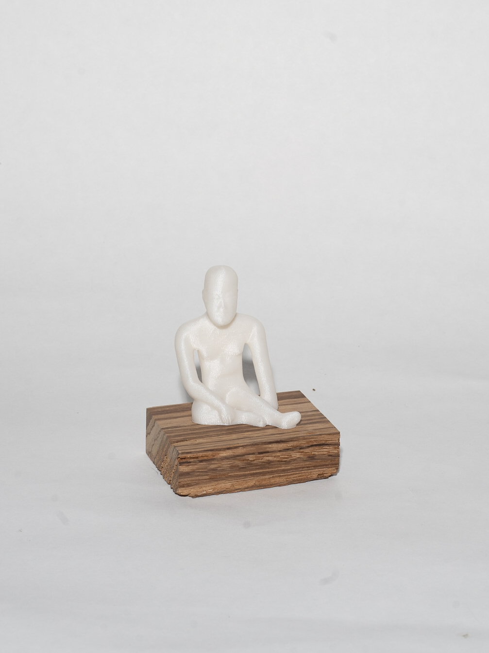 A 3D human figure sits on a rectangular wooden block. The figure is entirely white with limited detail.
