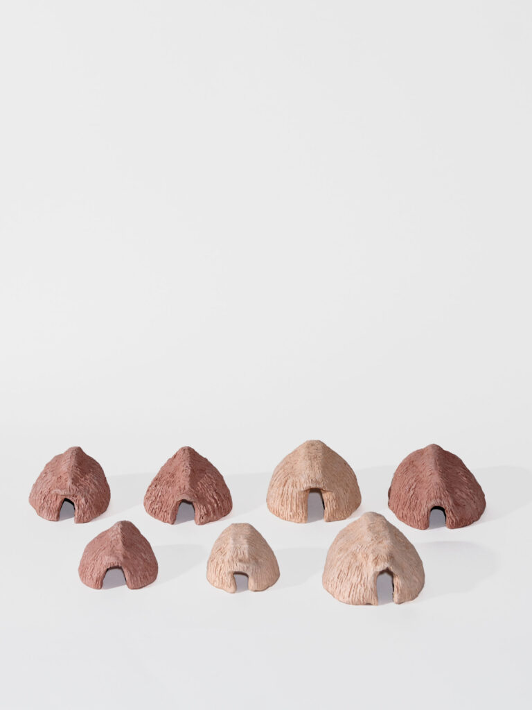 Seven 3D clay huts are on a white background in rows, three huts in front and four in back. They are simple half domes with an opening for a door.