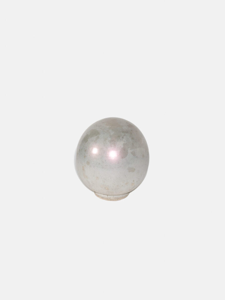 A silver and grey mottled sphere in front of a white background. The sphere reflects two circles of light and is on top of a circular stand.