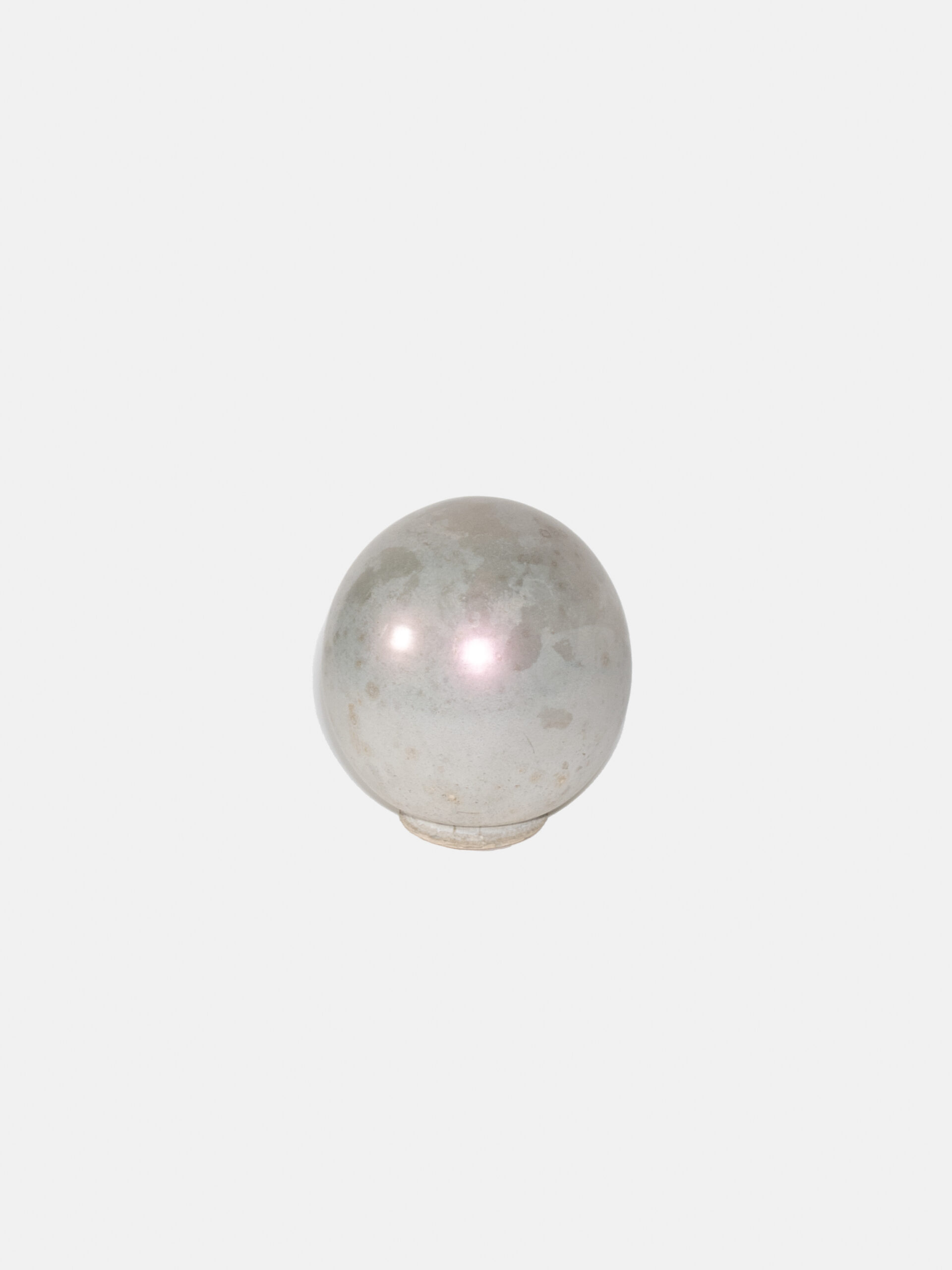 A silver and grey mottled sphere in front of a white background. The sphere reflects two circles of light and is on top of a circular stand.