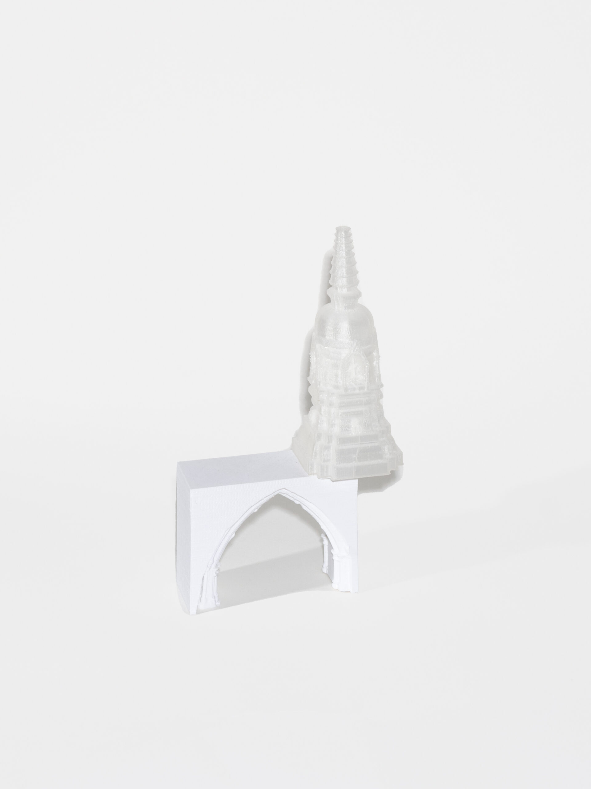 A 3D white rectangle with a cut out of a pointed holds up the top of a white tower. The tower sits on the edge of the rectangle.