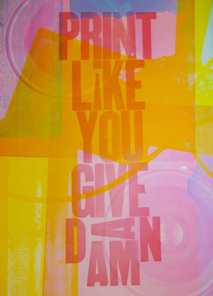 A brightly colored print reading: PRINT LIKE YOU GIVE A DAMN, in pink. The background consists of overlapping colors including orange, pink, blue and purple.