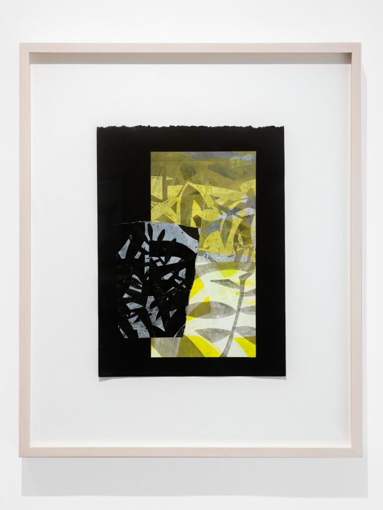 A small collage of prints on black paper. The print underneath is a vertical rectangle with abstract plant imagery in shades of yellow and gray and there is a small torn print in an amorphous rectangle on top with plant-like imagery in black on light blue-gray. It is in a blonde wood frame.