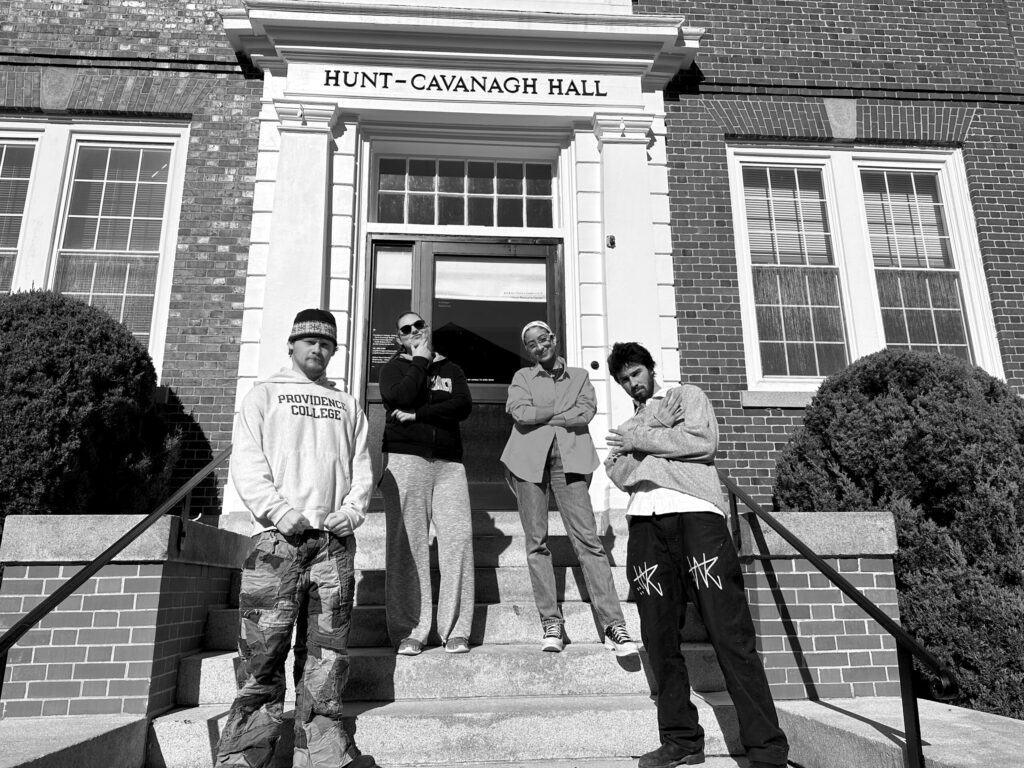 Black and white photograph of four students sitting on the front steps of Hunt-Cavanagh Hall at Providence College.