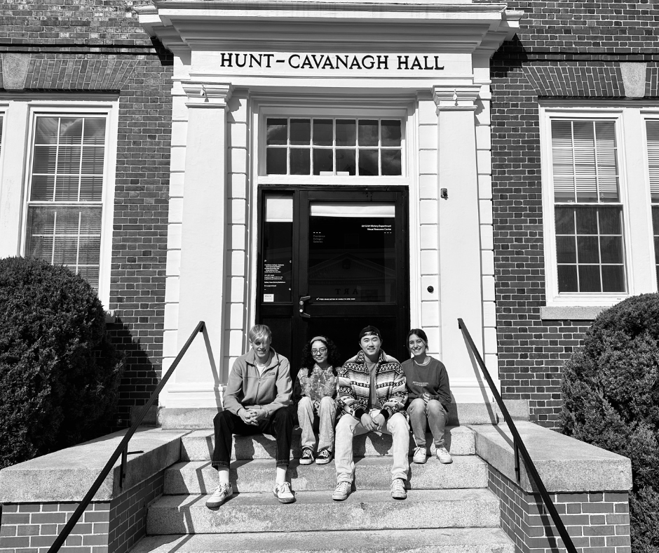 Black and white photograph of four students sitting on the front steps of Hunt-Cavanagh Hall at Providence College.
