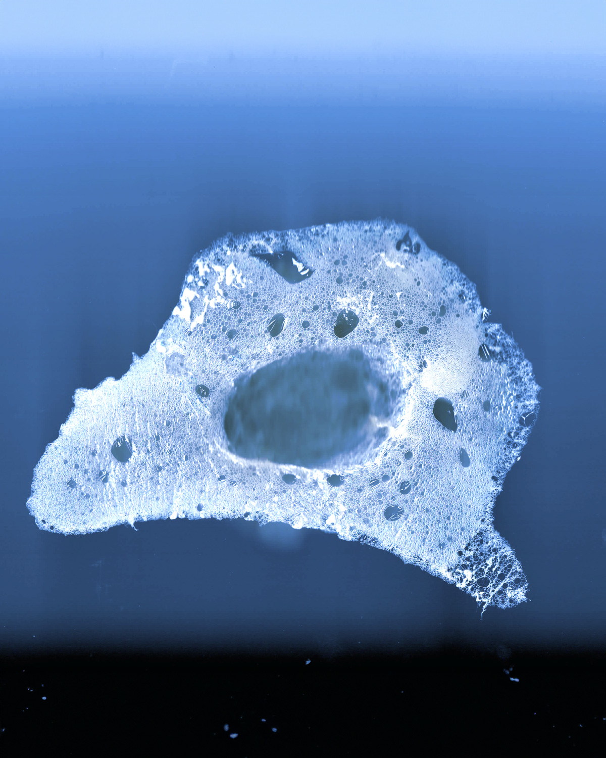An organic foam-like shape white with air bubbles in front of a gradient background, going from black to blue.