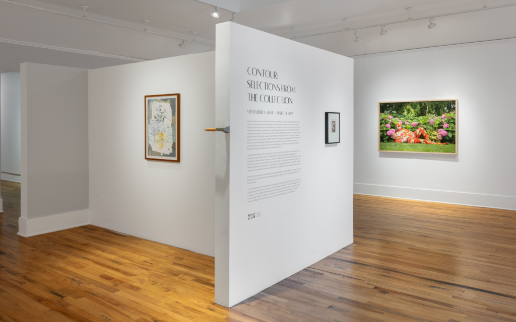 View of the entrance to the gallery space for Contour: Selections From the Collection. A white wall includes the name and information about the exhibition. On either side, artworks are hung on the walls.