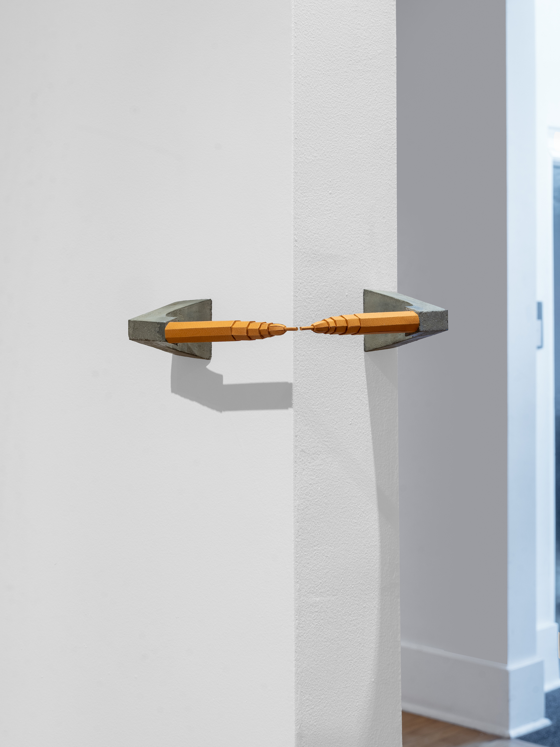 A sculpture with two brown skyscrapers facing each other horizontally. They are mirror images of one another, both mounted on stands of grey concrete.