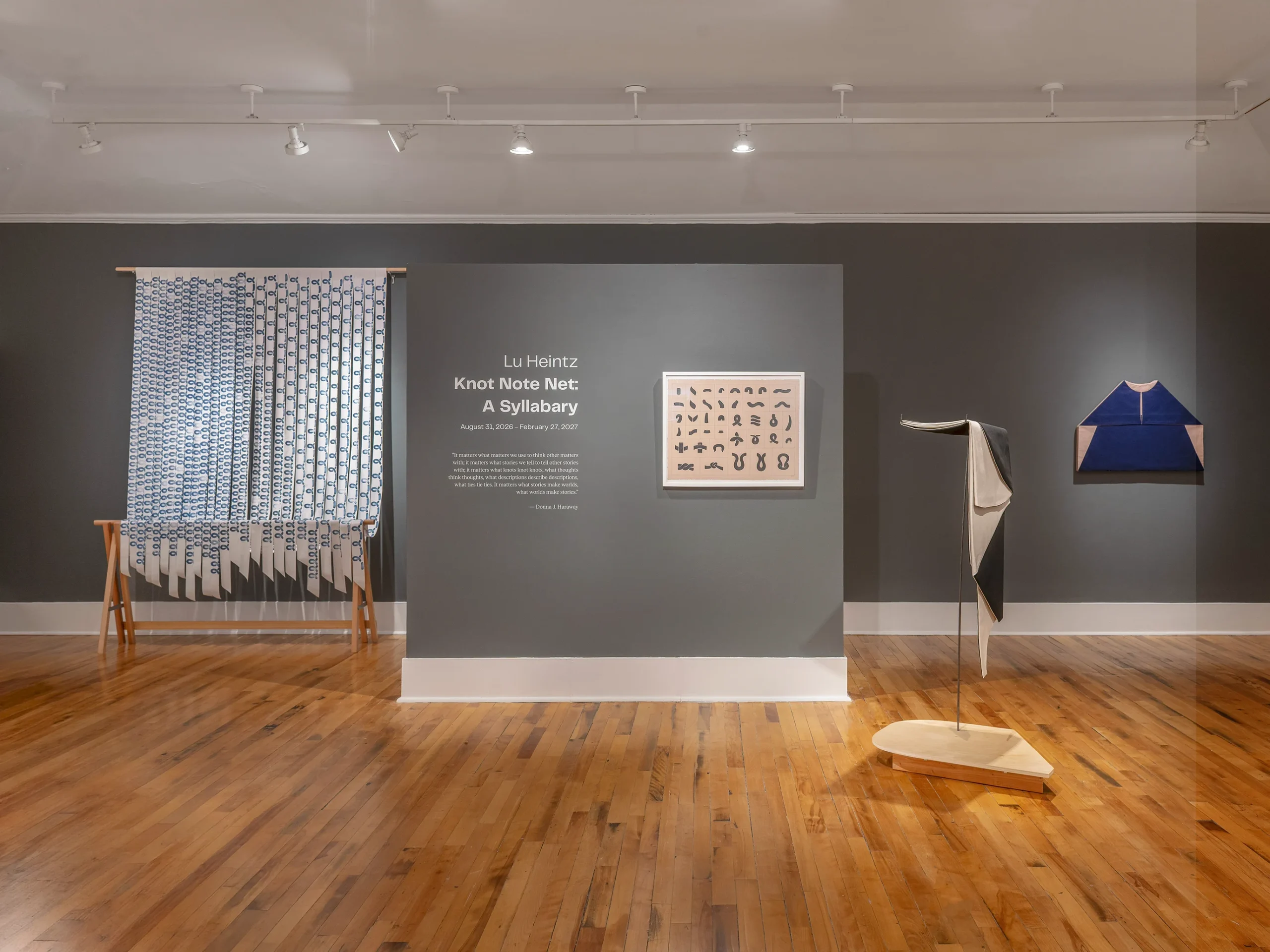 A gallery space with wooden floors, dark gray walls, and four exhibit pieces.