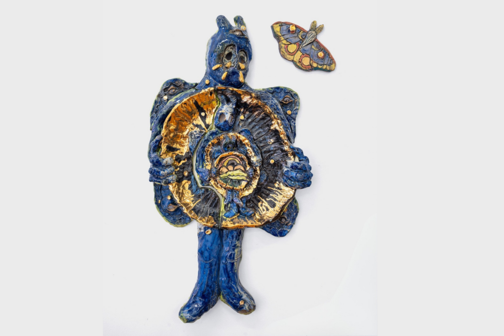 Blue ceramic figure with nesting worlds in torso and butterfly to the upper right of head.