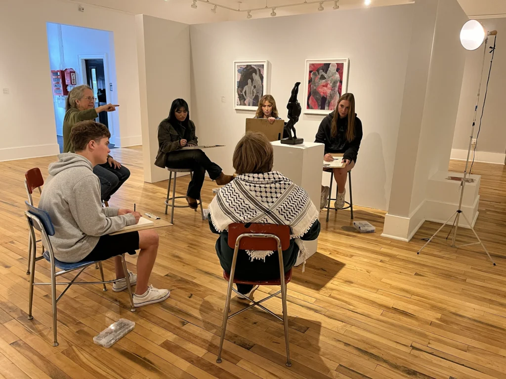 Educators sitting on chairs, in a circle, in a gallery.